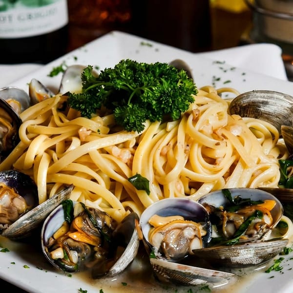 Linguine with clams and parsley on a white rectangular plate, with a wine bottle in the background.