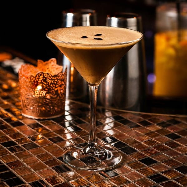 Espresso martini with coffee beans on a tiled bar next to a glowing candle.