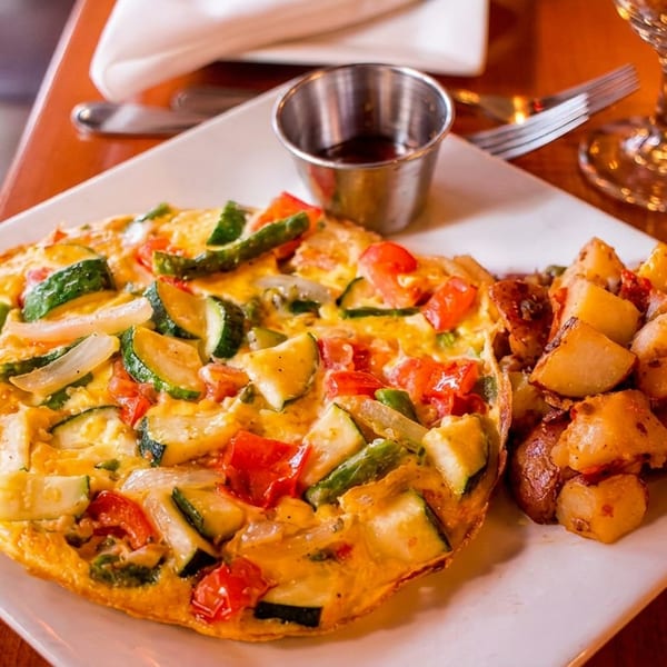 Vegetable frittata with zucchini, tomatoes, and onions, served with roasted potatoes on a white plate.