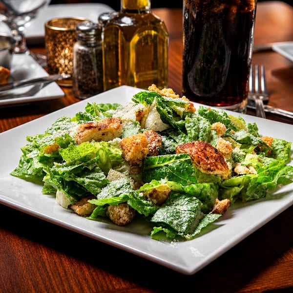 Fresh Caesar salad with grilled chicken, croutons, and parmesan cheese on a white plate.