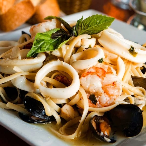 Seafood linguine with mussels, shrimp, and calamari, garnished with basil, served with bread.