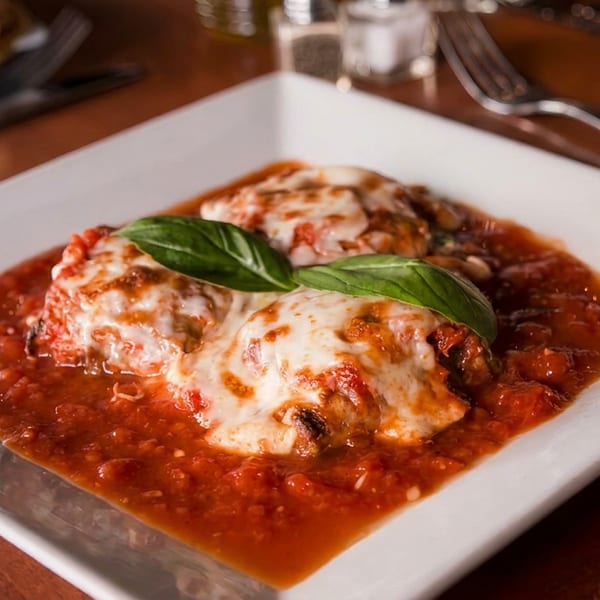 Two cheesy meatballs in rich tomato sauce, garnished with fresh basil, on a white plate.