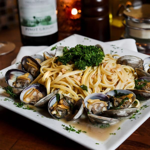 Linguine with clams, garnished with parsley, on a white plate with a wine bottle in the background.