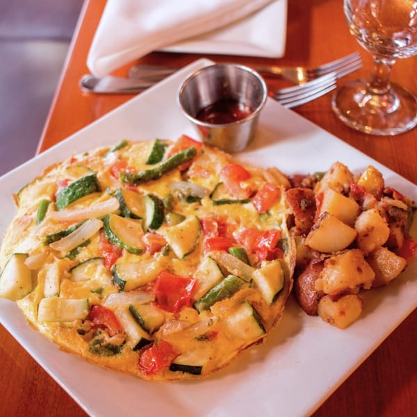 A vegetable frittata with zucchini, tomatoes, and onions, served with roasted potatoes and sauce.