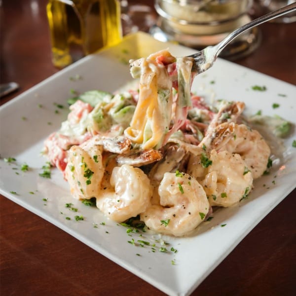 Creamy shrimp pasta with red and green vegetables, garnished with parsley, on a white plate.