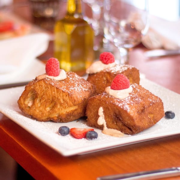 Three golden-brown Italian pastries topped with cream, raspberries, powdered sugar, blueberries, and strawberries.