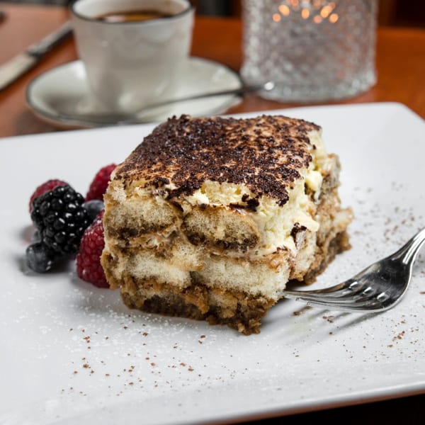 A slice of Mama Mia 44SW's tiramisu with berries and a fork on a white plate.