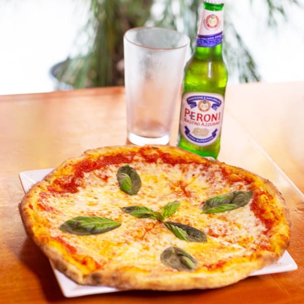 Mama Mia 44SW's Margherita pizza with fresh basil, a glass, and a Peroni beer bottle.