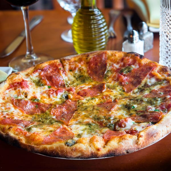 A Mama Mia 44SW pepperoni and pesto pizza, with a glass of wine and olive oil.
